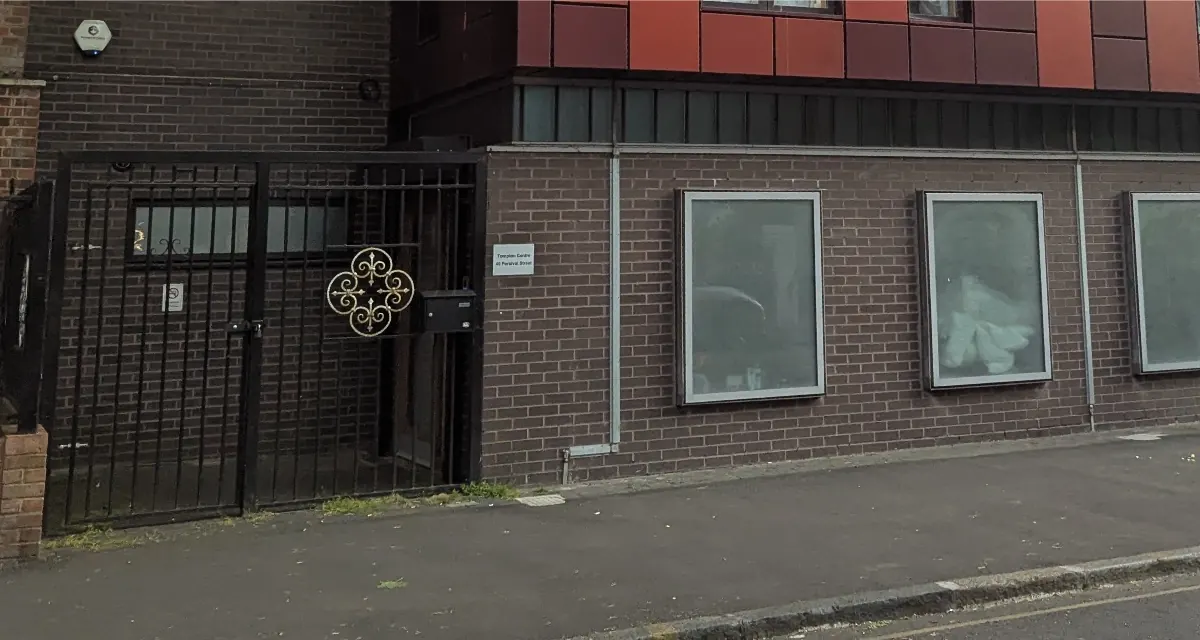 The Percival Street frontage of Tompion Community Hall: a
                locked iron gate beside a row of shuttered ground-floor windows,
                under the red cladding of the block above.